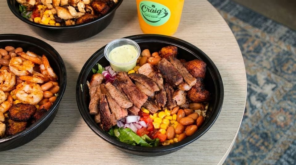Three bowls of food, one with steak, one with shrimp, and one with chicken, on a wooden table.