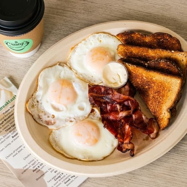 A full breakfast plate with three fried eggs, bacon, toast, and a side of mayonnaise from Craig's.
