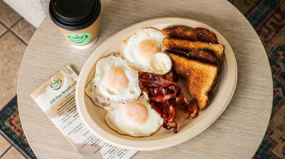 A full breakfast plate with three fried eggs, bacon, toast, and a side of mayonnaise from Craig's.