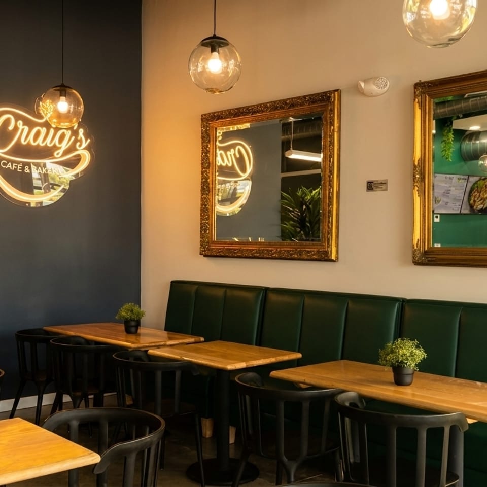 Interior of Craig's Cafe & Bakery with a neon sign, green booth seating, and wooden tables.
